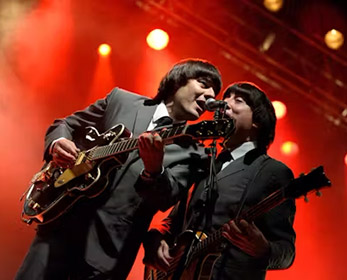 Beatles Tribute band playing guitars live on stage at a concert