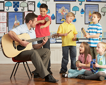 A teacher playing guitar to children.